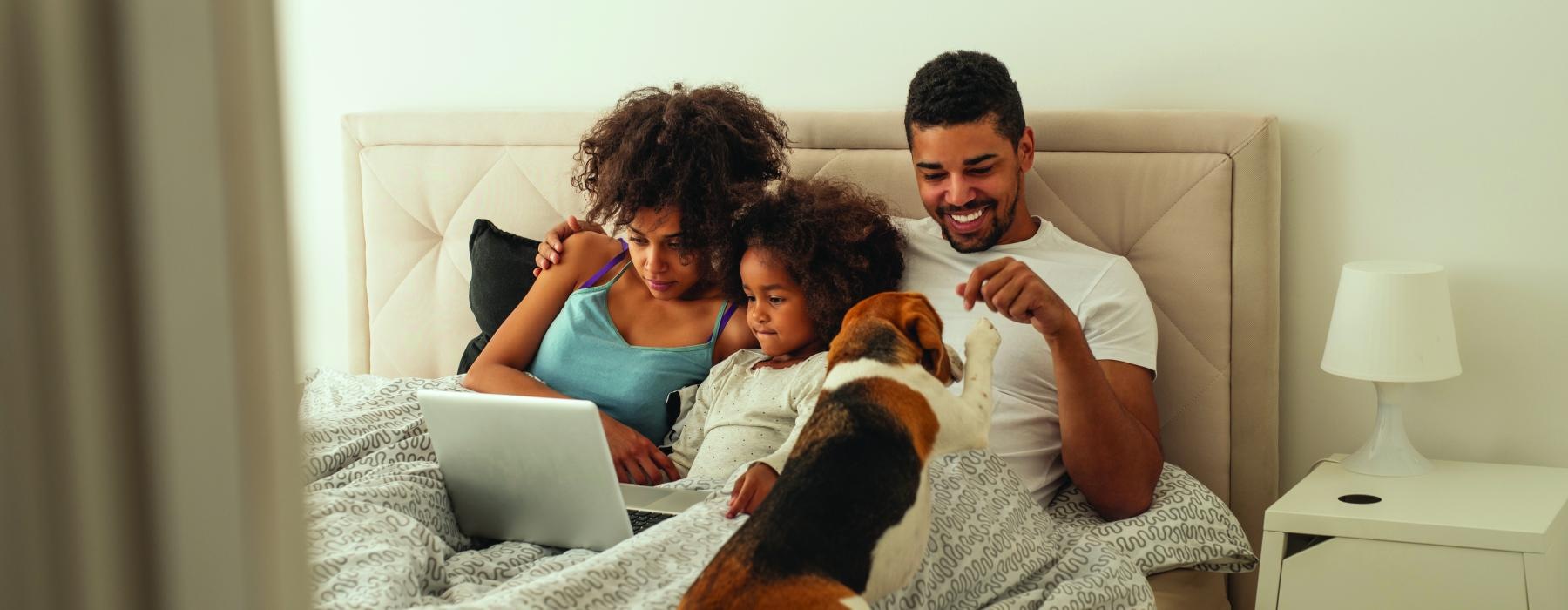 a family sitting on a bed with a laptop and a dog