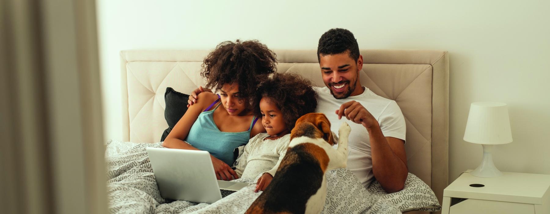 a family sitting on a bed with a laptop and a dog